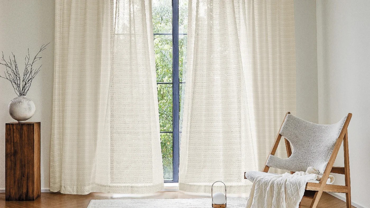 Light-filtering white curtains in a minimal interior with wooden side table and soft natural light.