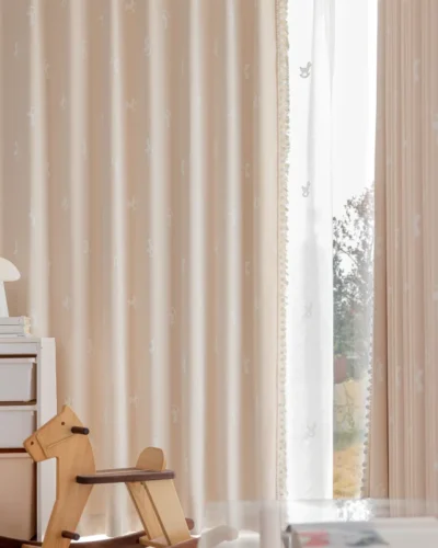 Rocking horse jacquard curtain in pastel pink softly filtering light in a kids’ room with wooden toys