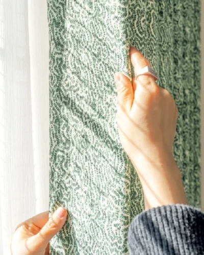 Hand touching green printed curtain to show botanical texture – Verdant Maze by Lemonhone