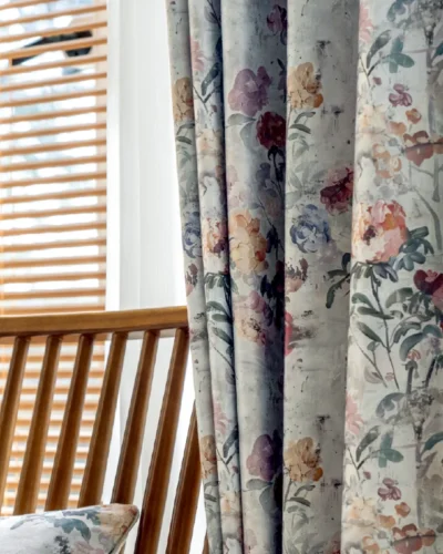 Close-up of botanical print curtains with soft floral design, styled beside wooden chair and window blinds.
