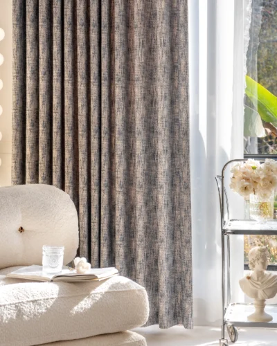 Living room with woven print curtain in deep indigo and beige, styled with neutral sofa and floral decor beside large window