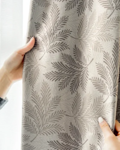 Elegant hand holding taupe botanical jacquard curtain with leaf pattern