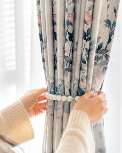Hands gently pulling Dreamy Meadow floral curtain, showcasing soft fabric texture and elegant draping