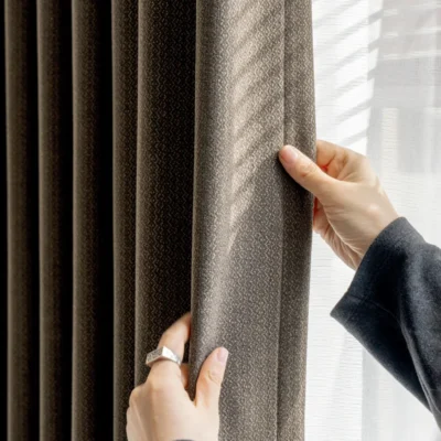 Close-up of hand touching Earthline Curtain in charcoal brown – textured fabric with soft light filtering by Lemonhone.