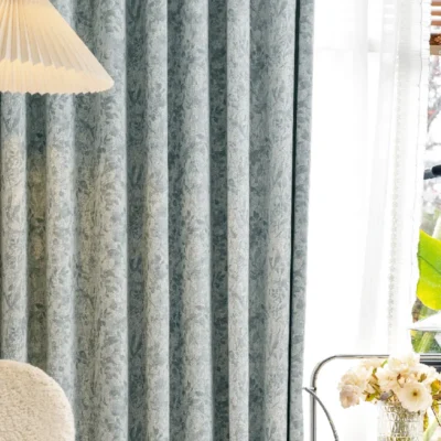 Botanical jacquard curtain in a soft blue tone hanging in a modern living room with wooden lamp and sheer