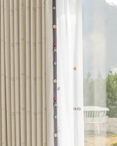 Detail view of yellow embroidered planets on kids' space-themed curtain, paired with sheer white layer