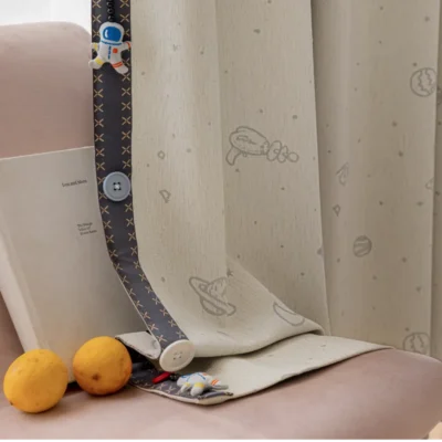 Bottom hem of embroidered kids curtain with planet and star design, shown with toys and sheer fabric lining