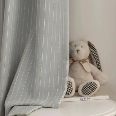 Close-up of Whisper Stripe Curtain in mist grey with vertical lines, styled with a soft toy bunny for kids’ room