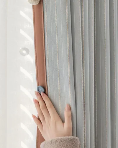 Hand touching Whisper Stripe Curtain in mist grey, highlighting soft texture and gentle drape by the window