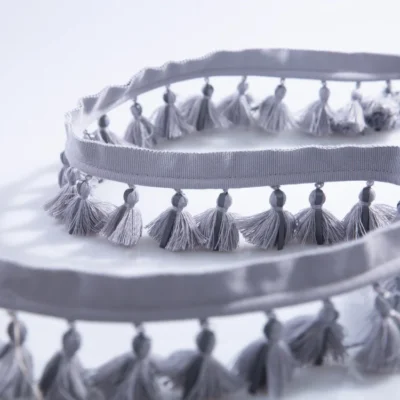 Side-by-side view of single-layer tassel fringe trims in gray blue and beige tones, showing color options