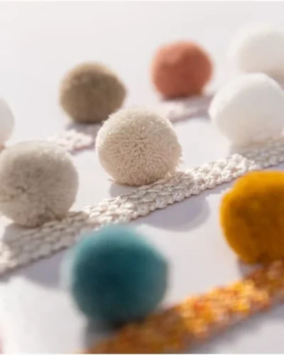 Assorted Eden pom pom trim colors in close-up view – ivory, taupe, teal, gold, and more
