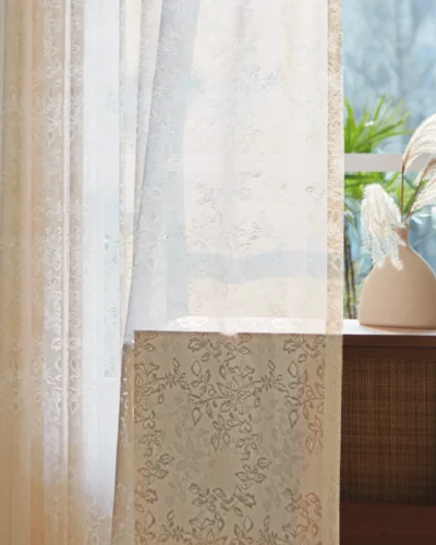 Close-up of floral lace sheer curtain with soft light and indoor plant in background