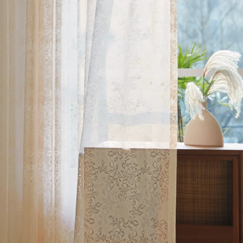 Close-up of floral lace sheer curtain with soft light and indoor plant in background