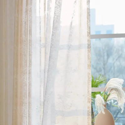 Sheer floral lace curtain hanging on window with soft natural light and indoor plant decor