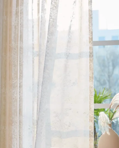 Sheer floral lace curtain hanging on window with soft natural light and indoor plant decor