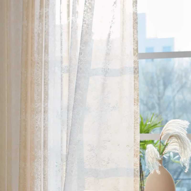 Sheer floral lace curtain hanging on window with soft natural light and indoor plant decor