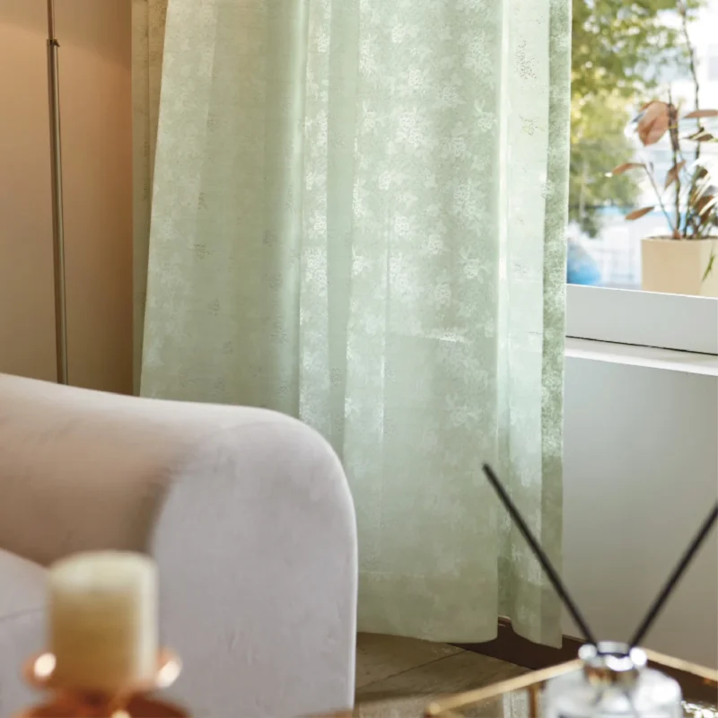 Olive Mist Curtain softly draping beside a sofa and window, filtering daylight in a cozy natural living space