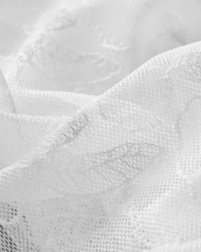 Close-up of white sheer curtain with delicate leaf embroidery texture