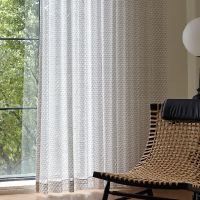 White jacquard sheer curtain hanging in a modern living space with natural light and a woven chair