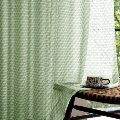 Close-up of green jacquard sheer curtain with geometric pattern next to a table
