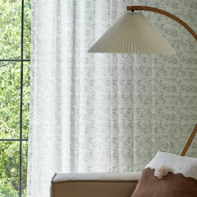 Dual-tone jacquard sheer curtain with leaf pattern softly diffusing daylight in a cozy bedroom corner.