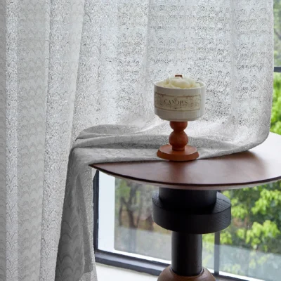 White jacquard sheer curtain softly draping beside a window with floral candle
