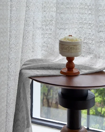 White jacquard sheer curtain softly draping beside a window with floral candle