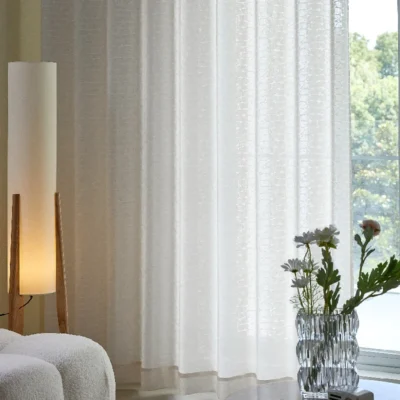 Echo Leaf curtain hanging in a softly lit living room with floral vase and lamp