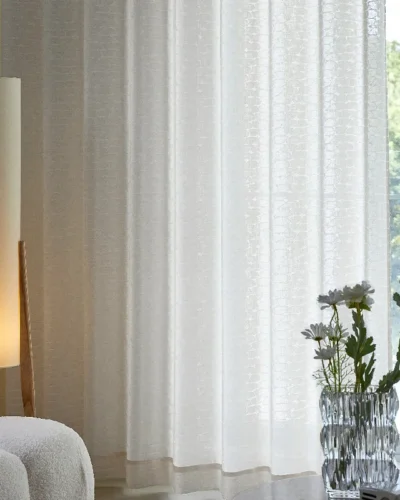 Echo Leaf curtain hanging in a softly lit living room with floral vase and lamp