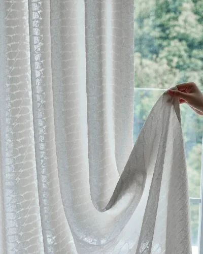 Close-up of hand lifting Echo Leaf Curtain to show double jacquard texture and soft light filtering