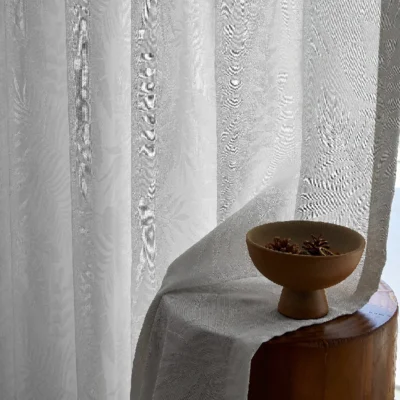 Close-up of sheer jacquard curtain with leaf patterns, softly draped next to a round wooden table