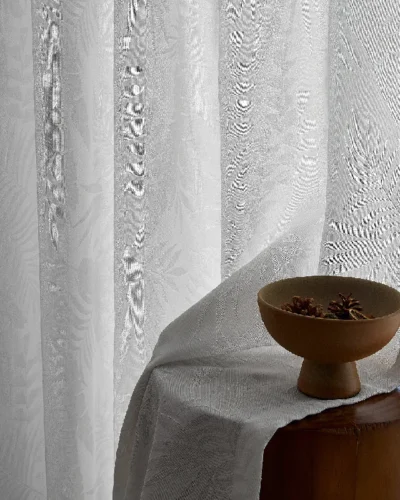 Close-up of sheer jacquard curtain with leaf patterns, softly draped next to a round wooden table