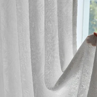 Botanic jacquard sheer curtain gently held by hand with daylight in the background