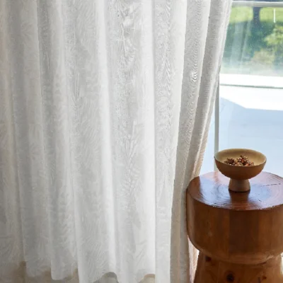 Sheer jacquard curtain with botanical leaf patterns, styled next to a wooden side table and window light
