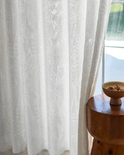 Sheer jacquard curtain with botanical leaf patterns, styled next to a wooden side table and window light