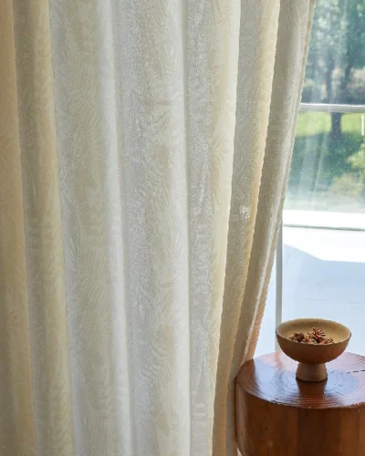 Elegant sheer curtain with botanical jacquard pattern, softly filtering sunlight in a bright interior