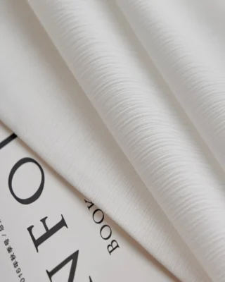 Fine Ridge Texture Curtain in soft matte ivory covering a wide living room window, paired with rattan chairs and modern furniture.