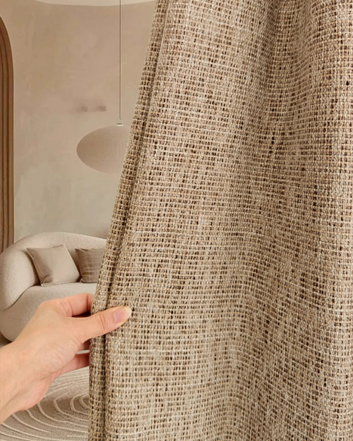 Hand holding cocoa jacquard linen-cotton chenille curtain fabric showing thick texture and weave