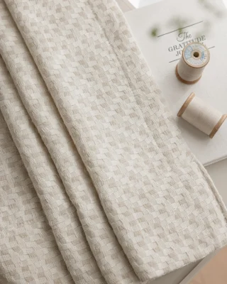 Basketweave texture curtain fabric folded on a surface with small decor pieces, soft woven drapes detail.