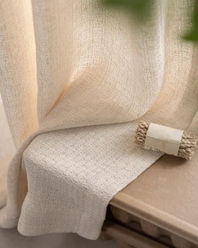 Textured curtain fabric draped over a wooden bench with a small decor piece, lattice texture curtain detail in a calm living room.
