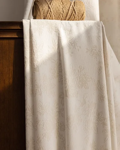 Warm beige floral jacquard curtain draped over a wooden cabinet in soft sunlight.