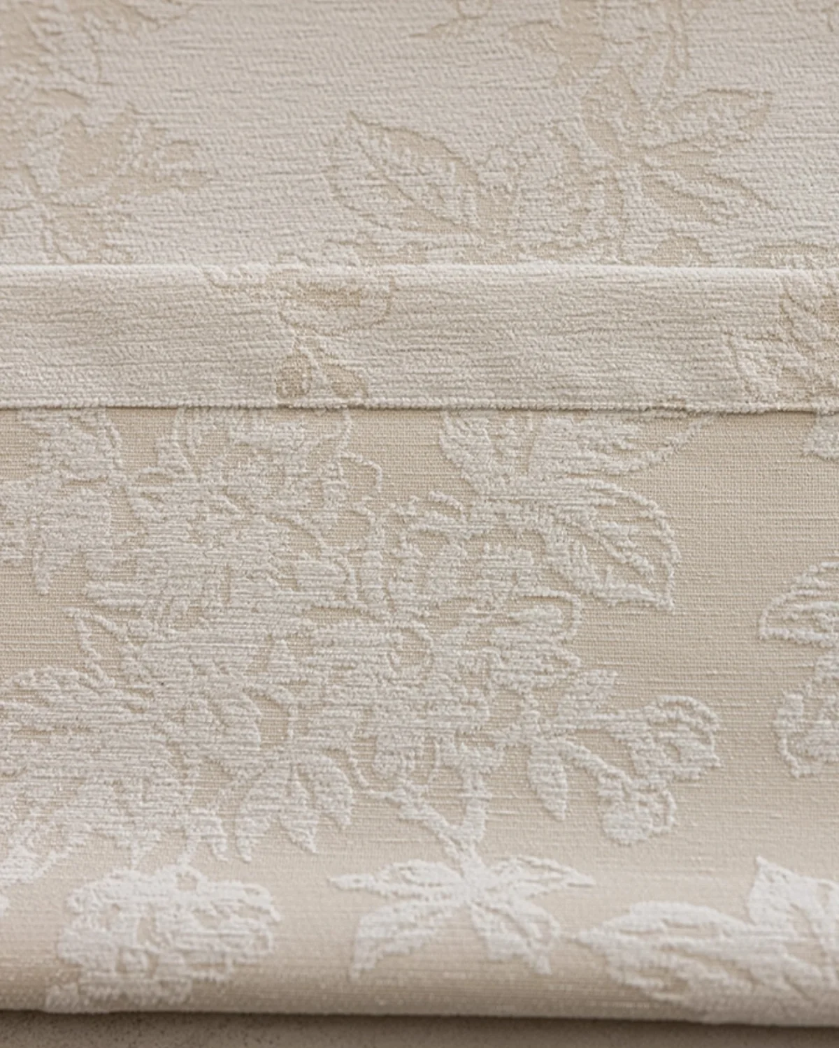 Close-up of warm beige floral jacquard curtain fabric with raised botanical pattern.
