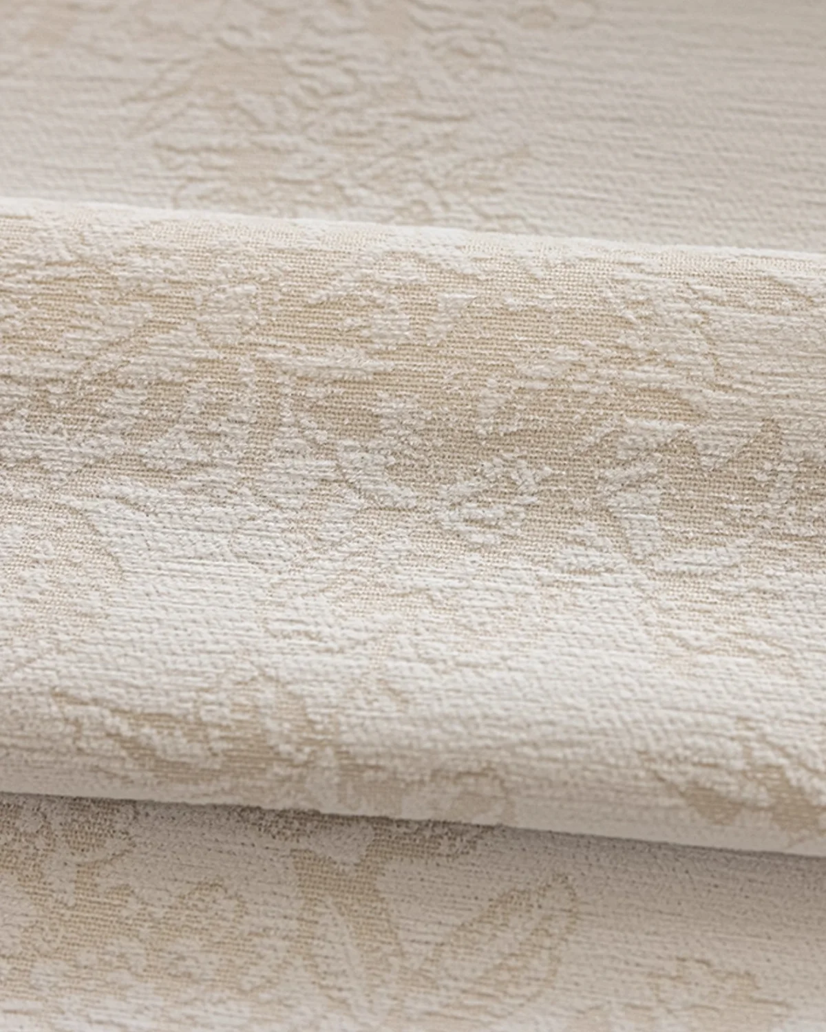 Warm beige floral jacquard curtain fabric folded in soft layers, showing subtle raised pattern.