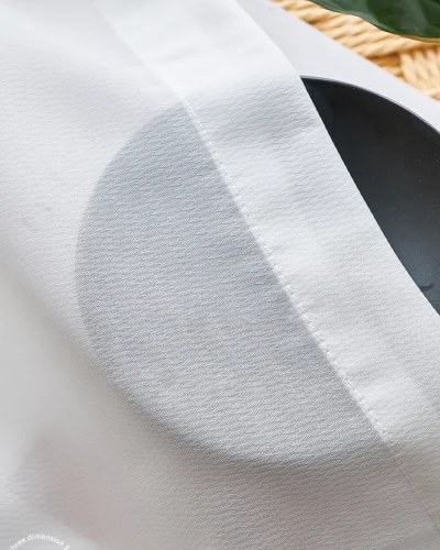 Soft white herringbone sheer curtain draped over a round grey cushion or plate on the window sill.