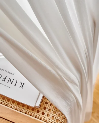 Fine Ridge Texture Curtain in soft matte ivory pooling on the floor beside a rattan chair and magazine.