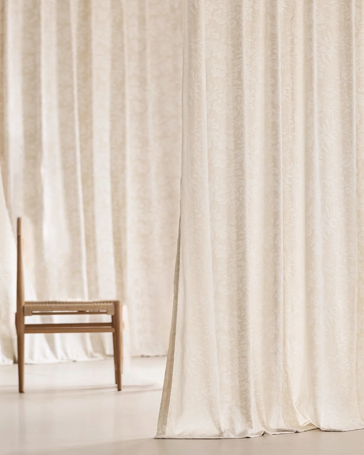 Blossom Whisper sheer curtain in beige floral jacquard hanging to the floor beside a simple wooden bench