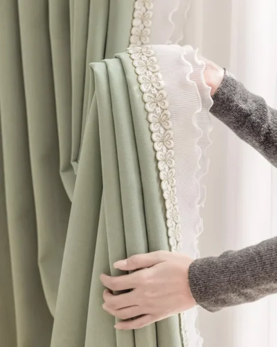 Hand holding sage green curtain to show floral lace trim and soft drape texture