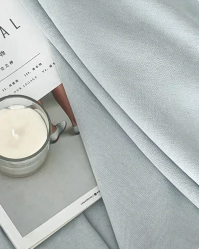 Close-up of cool grey blackout curtain fabric with smooth matte texture, styled with a book and candle