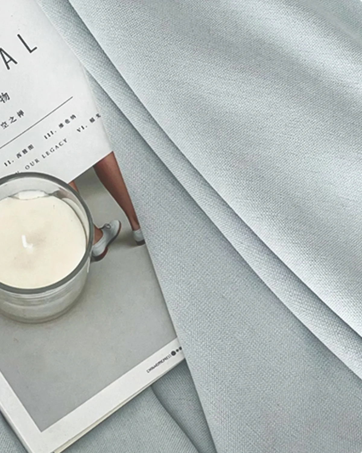 Close-up of cool grey blackout curtain fabric with smooth matte texture, styled with a book and candle