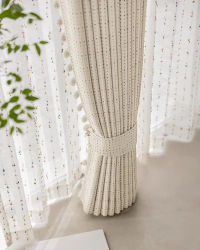 Tied-back Confetti Pom Pom Curtain showing soft pleats, multicolour dotted weave and light filtering through the window.